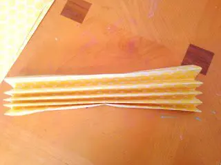 A folded piece of 12x12 scrapbook paper lays on a wooden table top. This is the first step in making rosette paper fans.