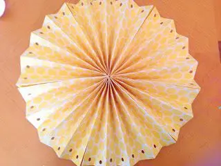 A round rosette fan made of yellow and white scrapbooking paper. Each edge has a hole punched into it. 