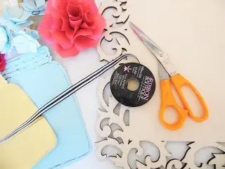 Craft supplies gathered for making a flower wall art craft include mason jar cut-outs, scossors, a paper flower and a decorative wooden frame. 