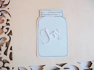 The word "Joy" has been glued to a cut-out of a blue mason jar on a wooden frame. 