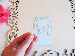 Abbi Kirsten holds  "Joy" in her hand, ready to glue the word to the mason jar cutout which rests on unfinished wooden frame. 