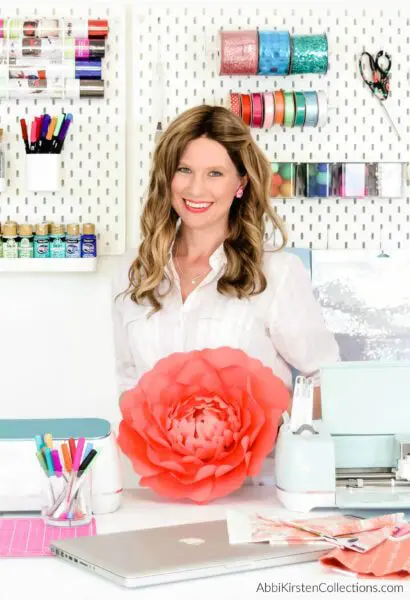 Abbi holding a coral paper flower in her work studio. 