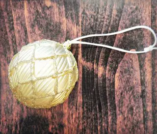 A round gold ornament with gold lattice and a white string in the top on a wood table. You can learn to dress up your ornaments using paper flowers.