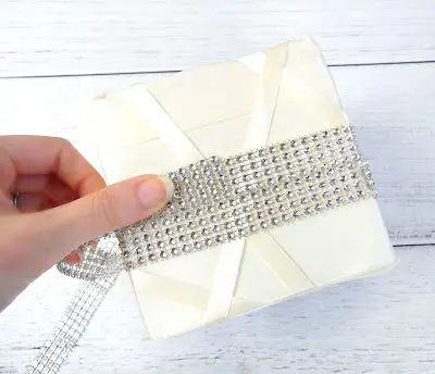 Abbi Kirsten's hand wraps rhinestone ribbon around the center of ribbon covered floral block to add a sparkle to the DIY wedding centerpiece craft.