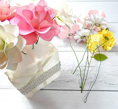 Blooming paper flowers have been added to the ribbon-wrapped floral cube, while additional stemmed paper flowers lay on the right, ready to be part of the wedding centerpiece arrangement.