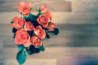 A bird's eye view of a bouquet of orange flowers blooming over their green leaves. An out of focus wooden table top is below. Baby shower favors are great crafts. 