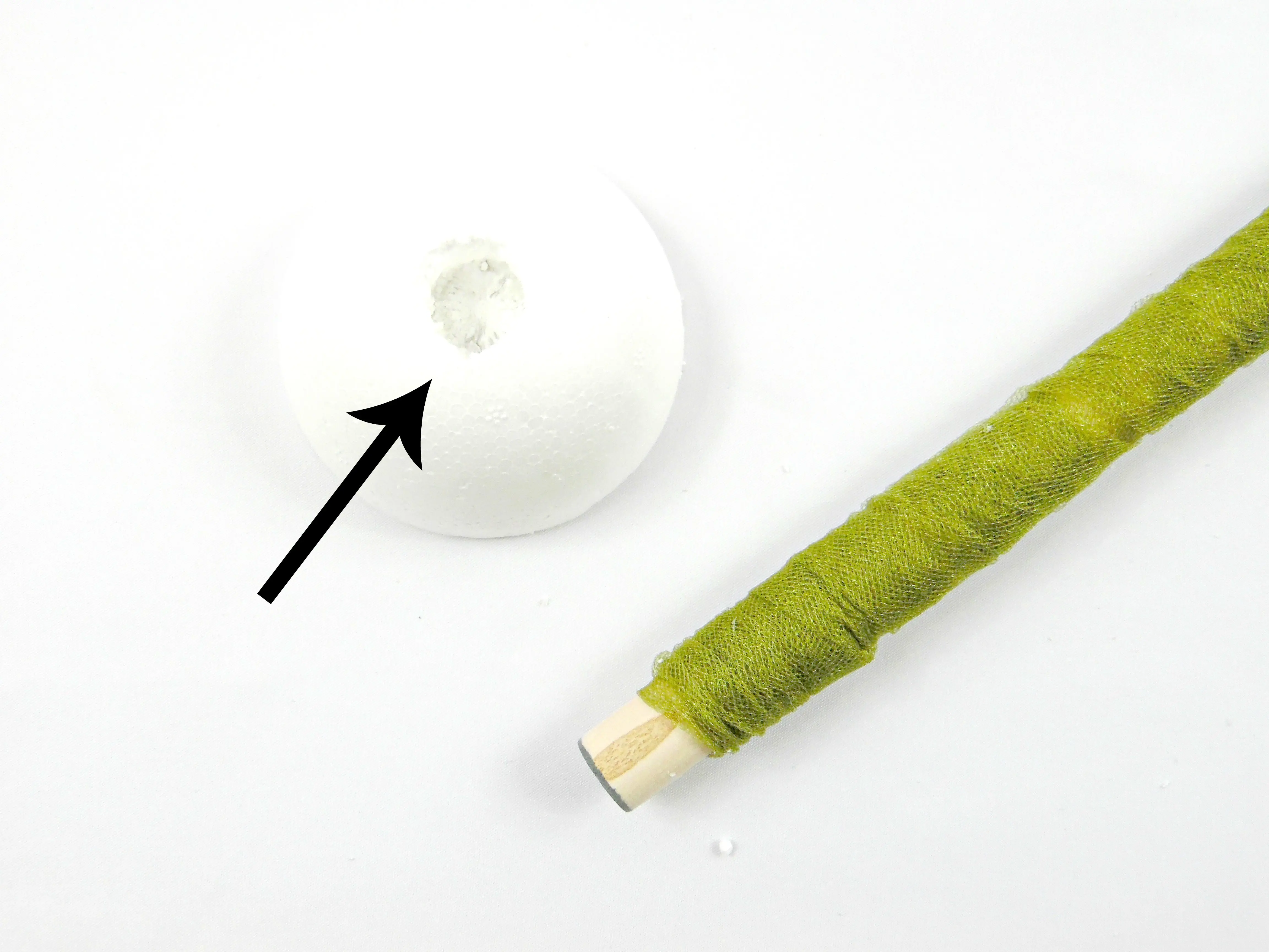 A foam ball, cut in half, has a deep dowel-sized hole in its center. Using the wooden dowel to carve out this hole is step 3 in the giant paper flower stem tutorial.