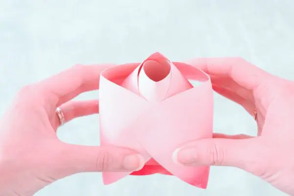 Abbi holds a pink, curled Alora paper rose center bud in her hands. 