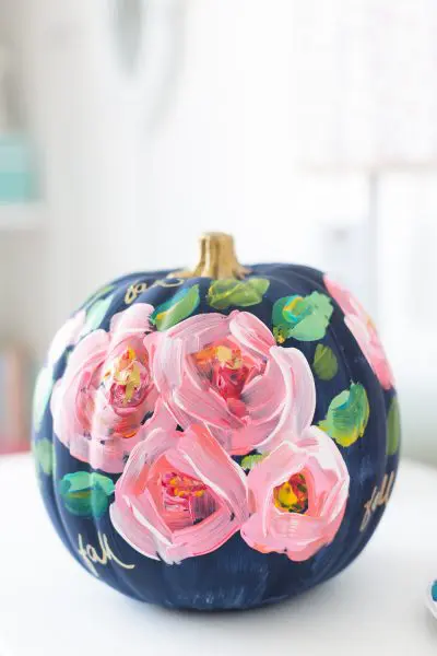 A medium sized craft pumpkin is painted navy blue with pastel pink flowers and green leaves on the front.