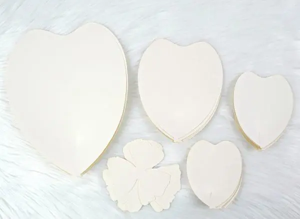 Five stacks of white paper petals are on a table ready to be made into a giant DIY paper Bella Rose flower. 