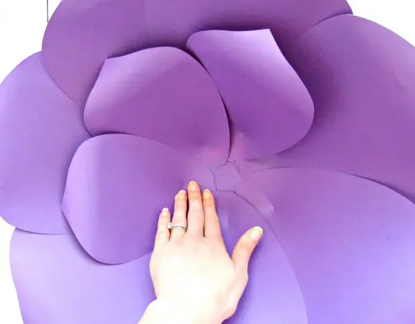 Abbi Kirsten's hand holds down the second layer of smaller purple paper petals that have been laid inside the outer layer of this giant paper flower.