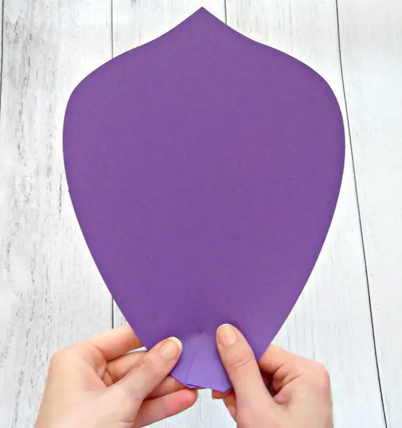 A closeup of Abbi Kirsten's hands holding two sides of a paper petal together to form a curl at the base. The giant purple paper petal is part of the assembly of a giant paper flower cut by a Cricut cutting machine.