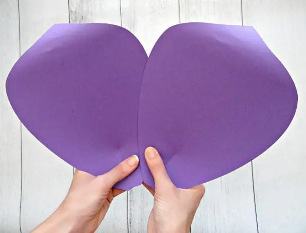 Abbi Kirsten holds two giant purple paper petals to use as the outer layer of a giant paper flower. The ends have been curled using a wooden dowel, which helps the paper flower look like it is blooming.