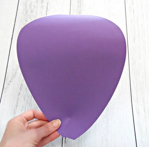 Over a white, distressed wood table, Abbi Kirsten's hand is seen holding the base of a finished purple paper petal cut by Cricut.
