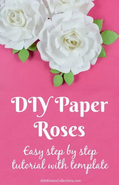 Three white paper roses with green leaves on top of a hot pink workstation.