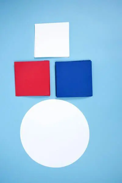 The paper supplies you need to make a Patriotic paper dahlia wreath. Stacks of red, white, and blue paper squares and a single white paper circle.