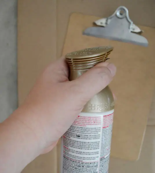 A woman's hand holds the top of a spray can, ready to paint the clipboard below.