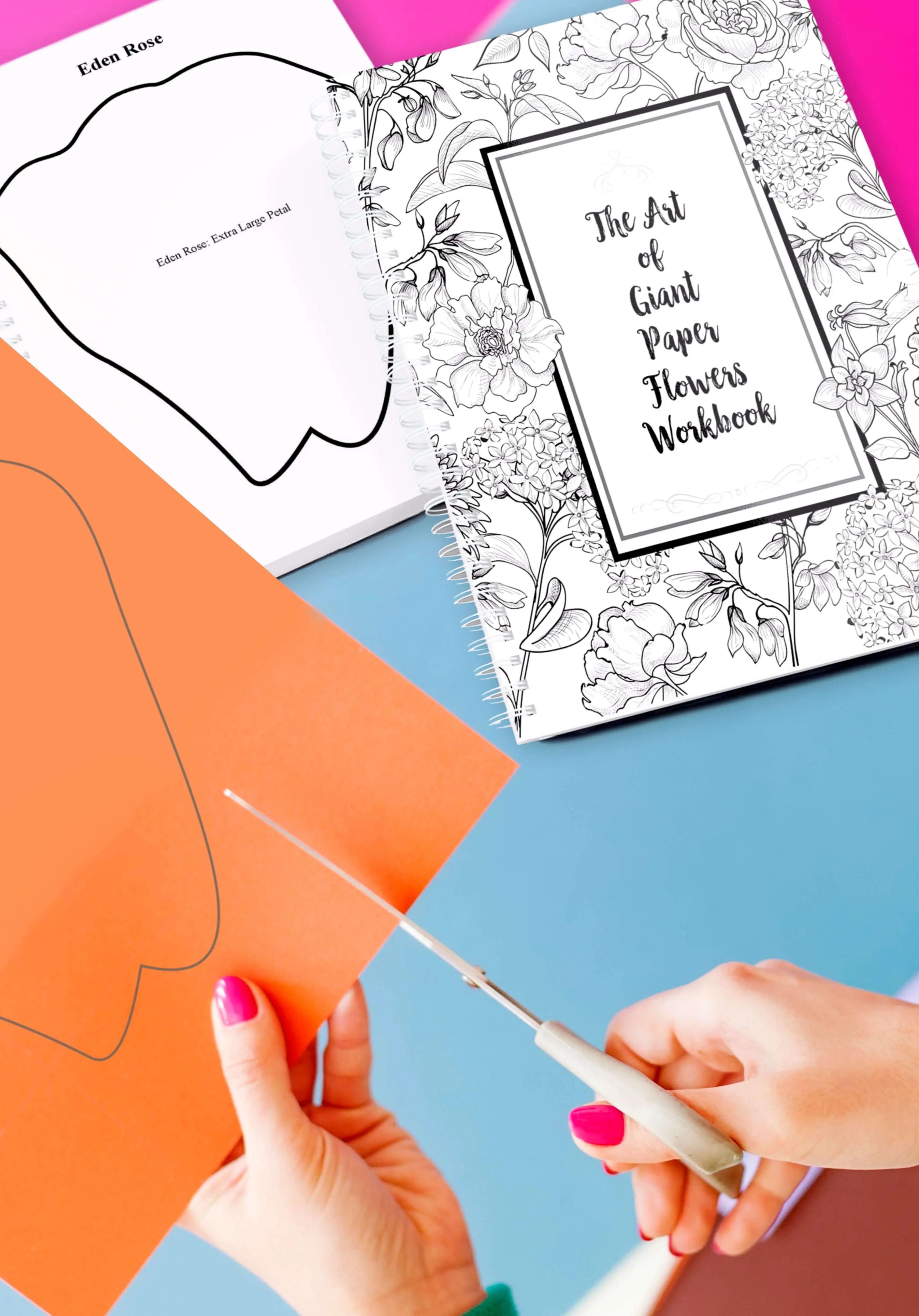 A black and white covered workbook sits on a table along with colorful sheets pf paper, each with a paper flower template outline printed on it. The book cover has text that says "the art of giant paper flowers workbook"