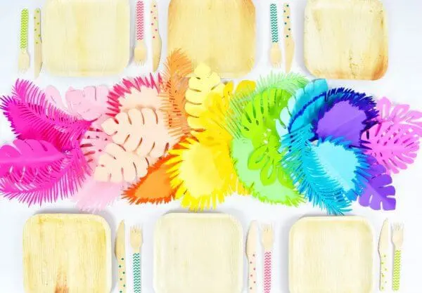 An overhead image of a bright Ombre Rainbow Paper Leaf Table Runner on a white table with bamboo plates and utensils. 