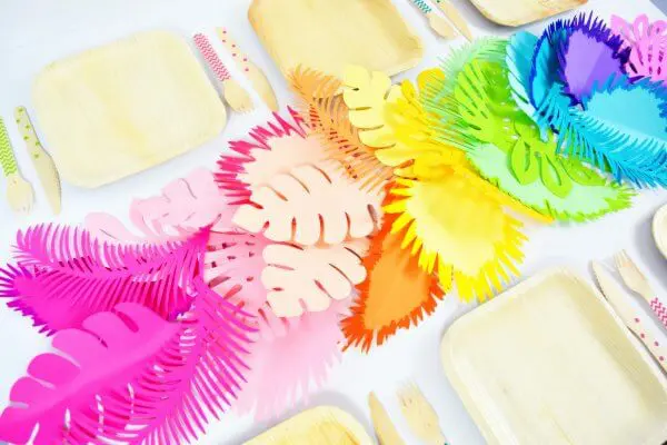 A bright ombre rainbow paper leaf table runner on a white table alongside bamboo plates and serving utensils. 