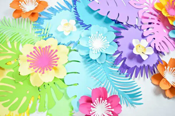 A variety of brightly colored paper flowers and leaves on a white table. 