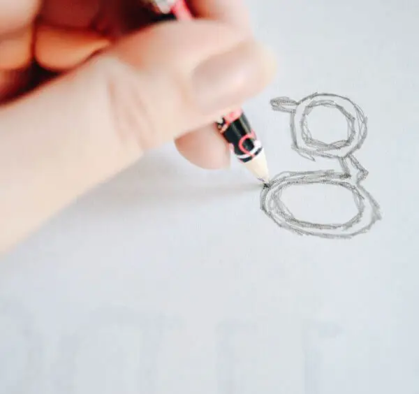 A hand holding a pencil drawing the lowercase letter "g" onto white paper.