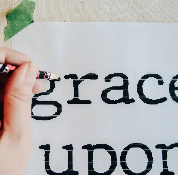 A hand holding a pencil tracing black text on a white paper.