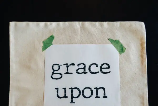 A piece of white paper that reads "grace upon grace" is taped with green tape on a cream colored pillow cover.