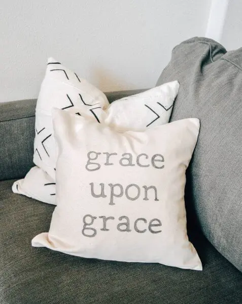Two cream colored pillows on a grey couch. One pillow has "grace upon grace" written on it.