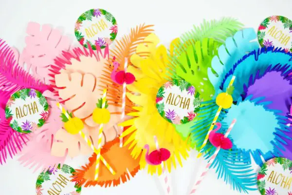 A brightly colored rainbow paper leaf table runner with tropical party favors scattered on top.
