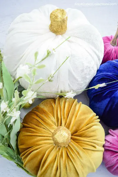 No-sew fabric pumpkins are made with velvet in a rainbow of fall colors. A gold glittery stem adds whimsy to these Fall decorations.