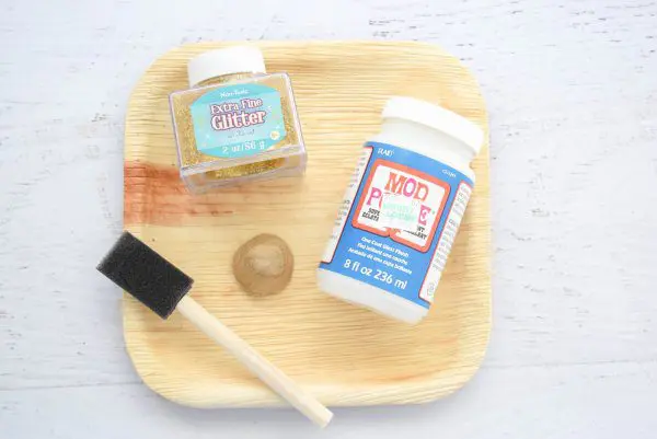 A tray holds a pumpkin stem, gold glitter, a sponge, and Mod Podge. These items are needed for the second part of the no-sew velvet fabric pumpkin tutorial.