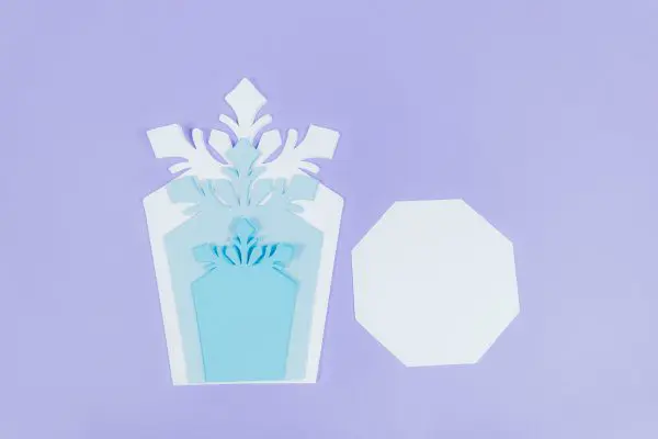 The different cutout pieces needed to make giant paper snowflakes. Three snowflake-like shapes in varying shades of blue papers, and one hexagon shape in light blue paper.