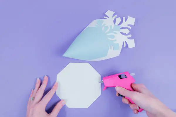 Abbi demonstrates how to add hot glue to the 8-sided paper snowflake base.