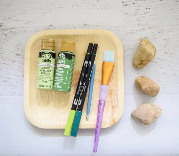 Rocks, paints, paintbrushes and markers on a table. 
