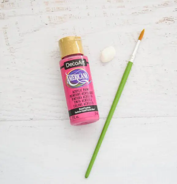 Pink paint and a green paintbrush laying on a white table.