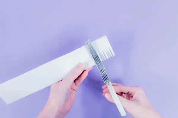 Abbi uses a fringe scissors to cut fringes into a single strip of light blue paper.