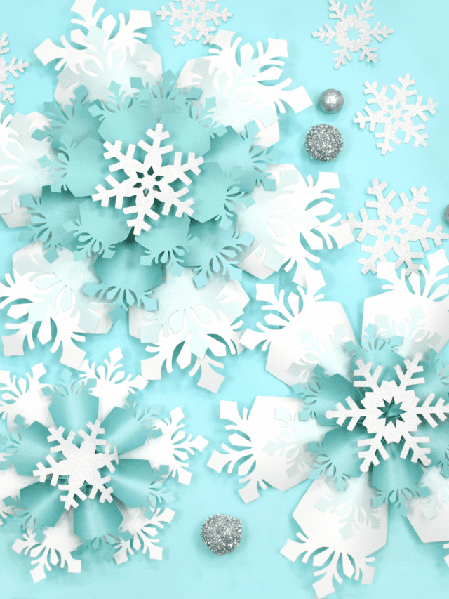 The image shows giant white and blue paper snowflakes made with Cricut. Get the templates on Abbi KIrsten Collections.