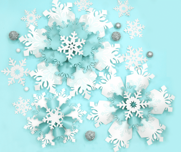 The image shows giant white and blue paper snowflakes made with Cricut. Get the templates on Abbi KIrsten Collections.