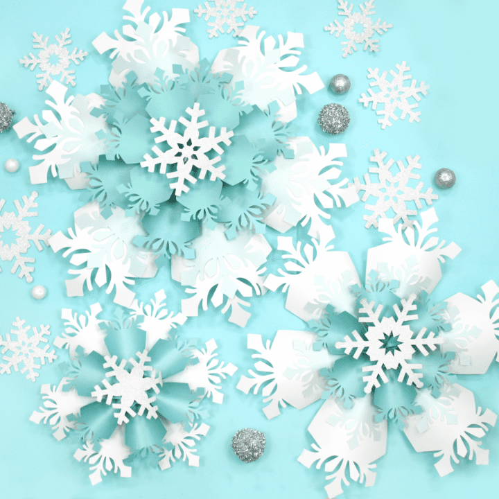 The image shows giant white and blue paper snowflakes made with Cricut. Get the templates on Abbi KIrsten Collections.