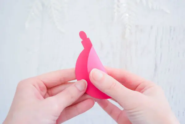 Abbi Kirsten's hand fold a pink paper ornament cutout in half. You can make 3D paper ornaments with Abbi's templates!