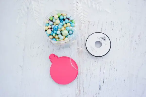 An unopened paper ornament, thread, and a jar of blue beads sit on a white wooden table-top. You can make your own 3D ornaments with this tutorial. 