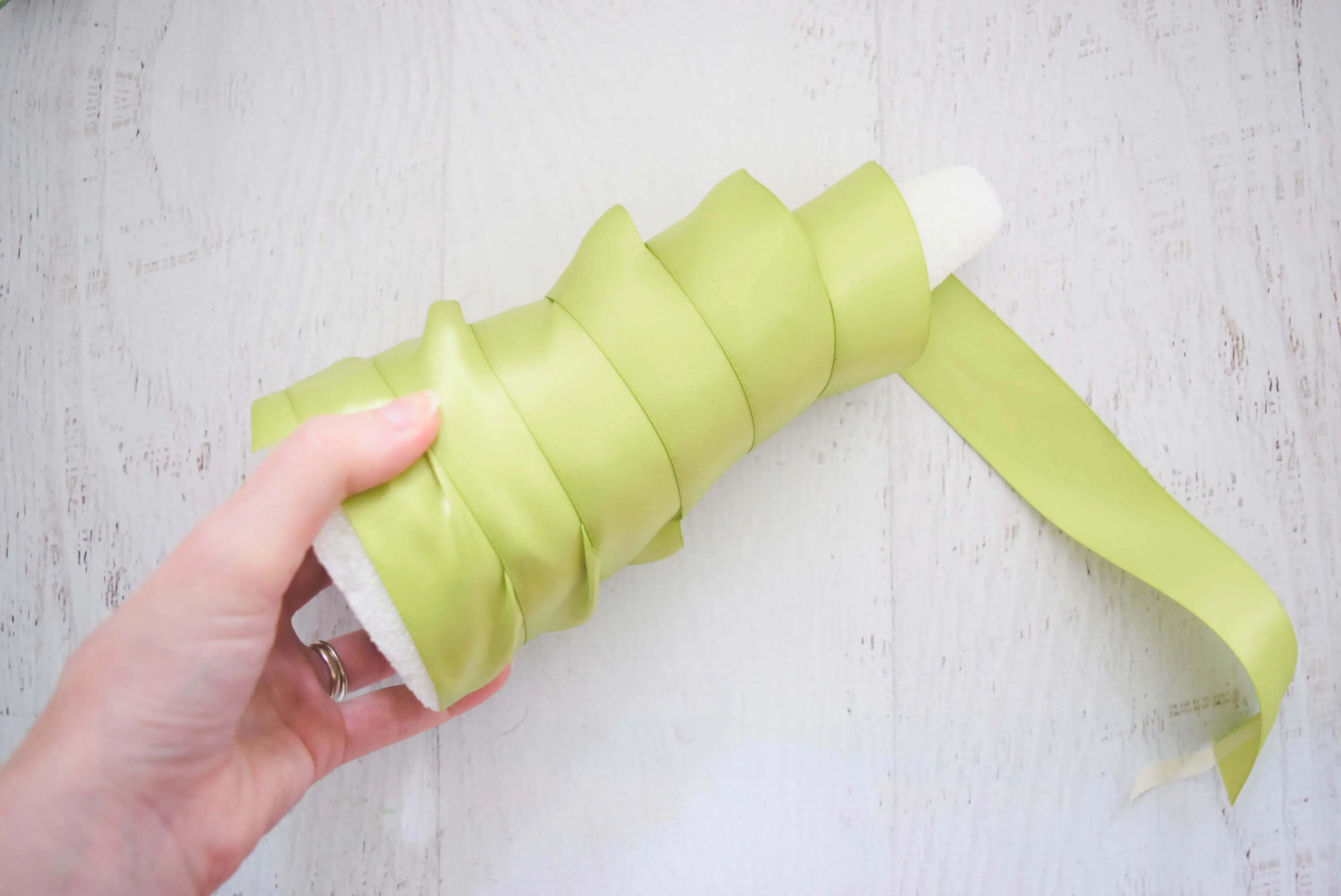 A white foam cone-shaped Christmas tree base wrapped with a light green ribbon.