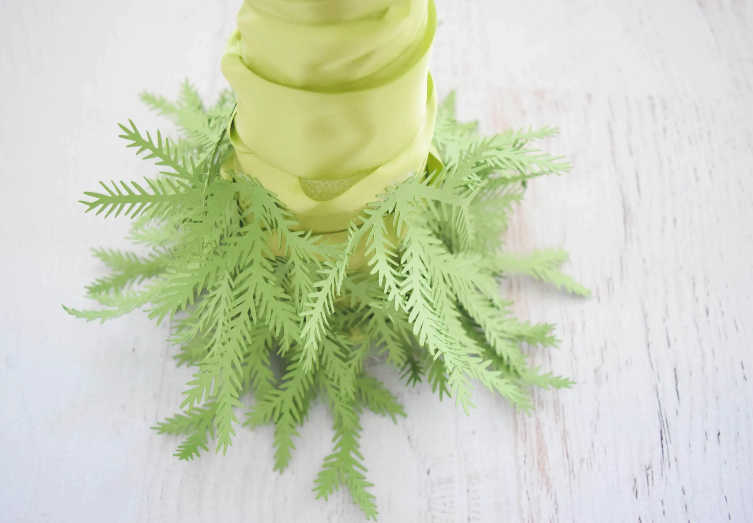 Many small green paper pine leaf branches are attached to the base of a green ribbon-wrapped foam cone, creating the bottom of the paper Christmas tree.