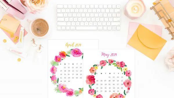 Calendar sheets with flowers around the days lay on a desk next to other office supplies. You can get your free 2019 printable calendar here.