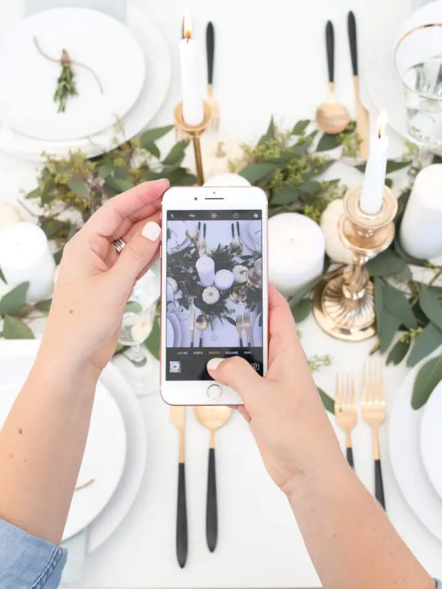 Hands holding a smartphone as it takes a photo of a floral centerpiece on a table arrangement