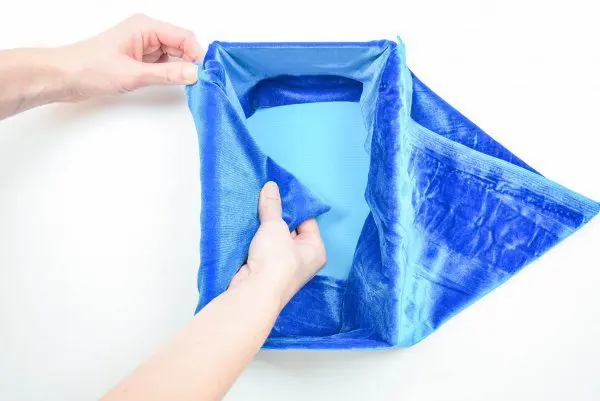 Blue velvet fabric is folded into a triangle on the outside of the cardboard storage box, then tucked in to the inside of the box.