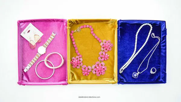 An overview of three shallow repurposed cardboard boxes wrapped in pink, yellow, and blue velvet. Each box is organizing sets of jewelry. You can make these DIY fabric storage boxes and clean up Marie Kondo-style.