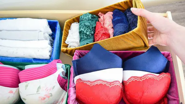 Abbi puts a mustard-colored velvet fabric-wrapped cardboard box into her undergarment drawer. There are other fabric covered storage boxes that are organizing parts of the drawer.