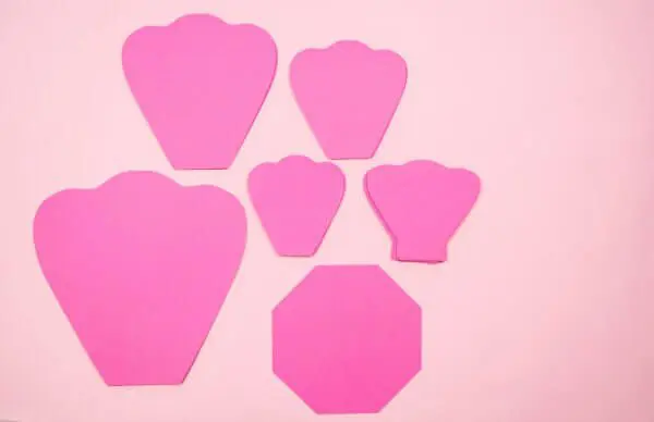 Five pink paper petals in different sizes are stacked next to a pink octagon paper base for making paper flowers like these Penelope roses.